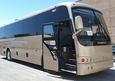 A tan charter bus with its door open, parked in a parking lot