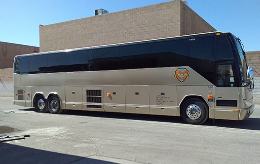 a tan charter bus parks in front of a Vegas building